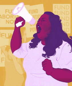 A lighter-skinned person with shoulder-length dark wavy hair shouts into a megaphone at a protest or rally. All around them are other abortion advocates, holding signs that read: “Fund abortion now!” and “Fund abortion Build Power!”.